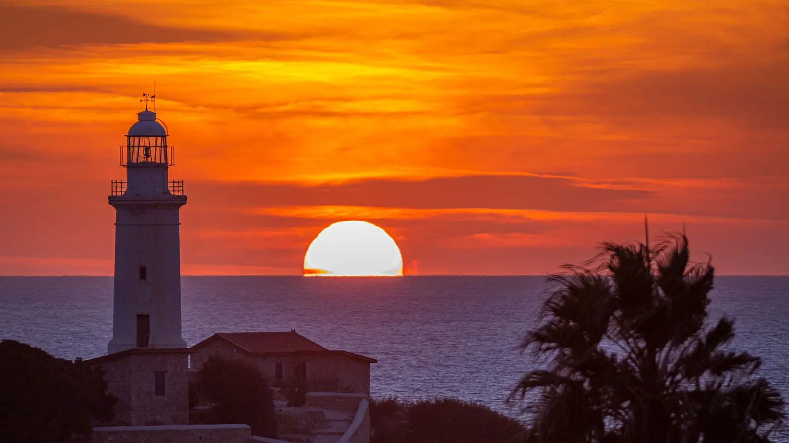 Paphos lighthouse at sunset, with the sun setting over the sea