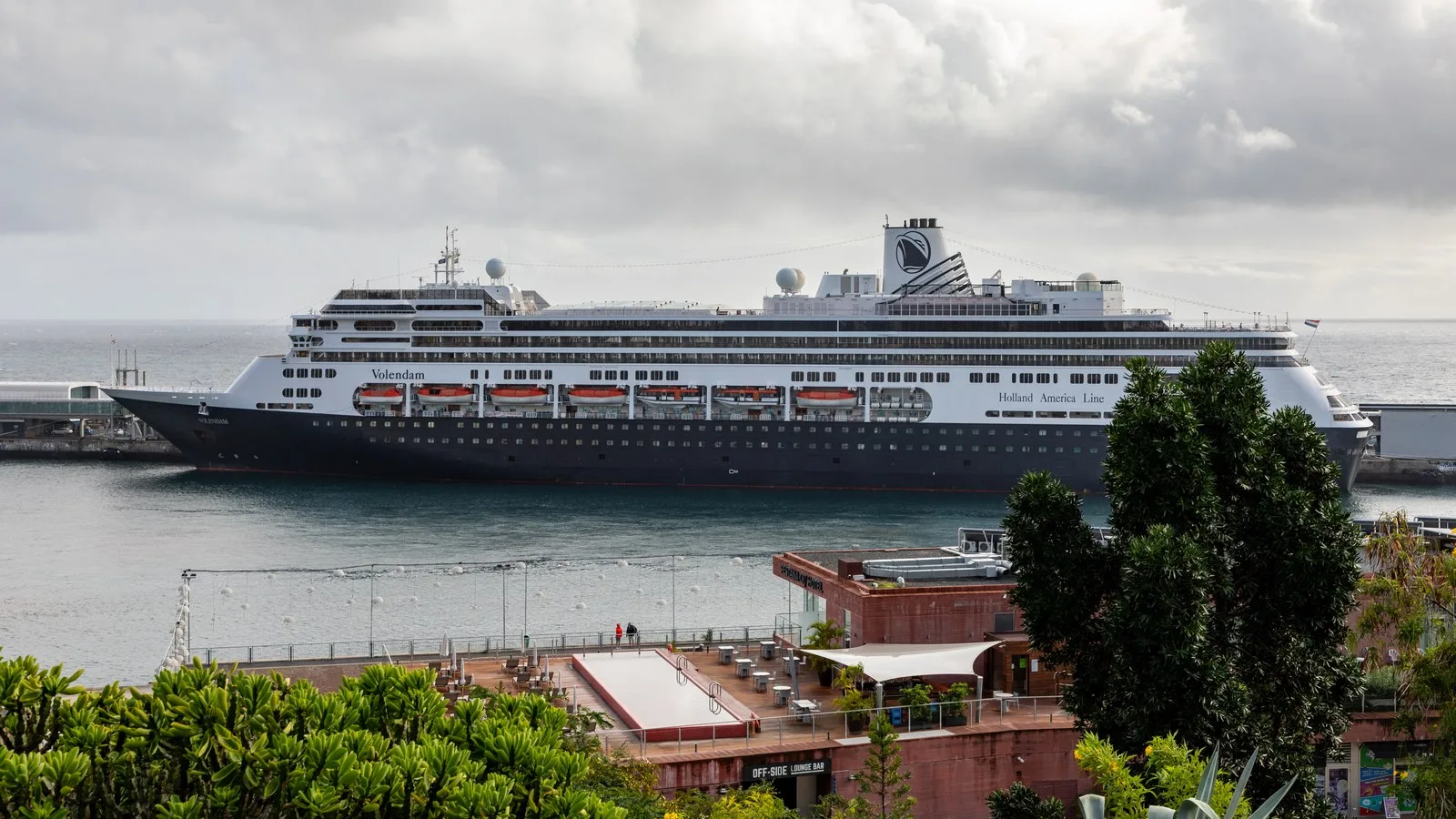 Portul din Funchal, Madeira, la amurg, cu nave la chei, luminile orașului pe golf și dealurile verzi în spate.