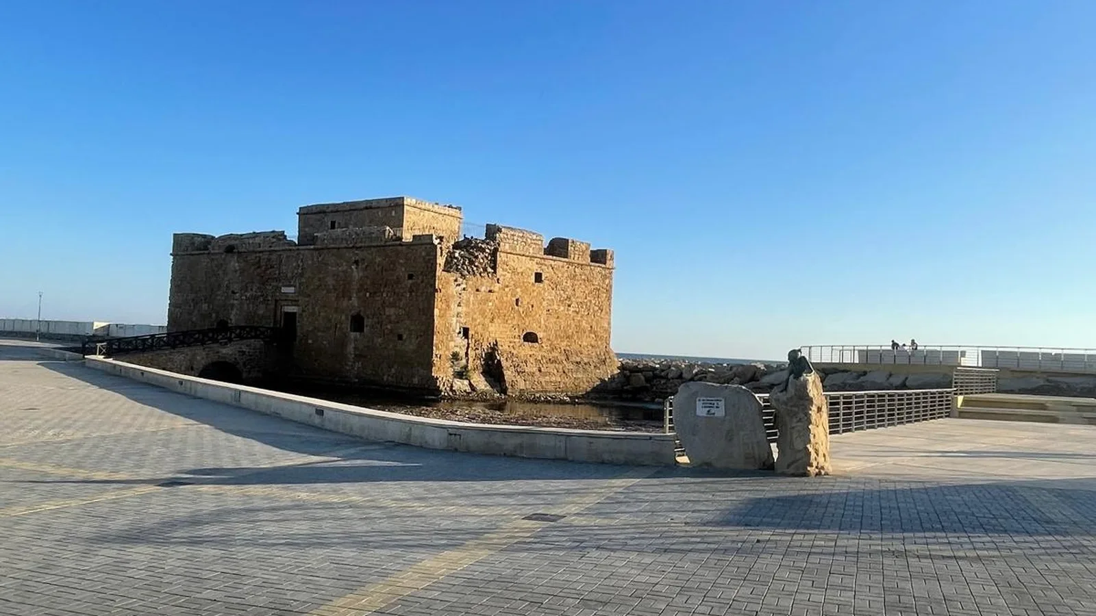 Die mittelalterliche Hafenburg von Paphos, Zypern, eine steinerne Festung am Ende der Mole unter klarem Himmel, das Mittelmeer dahinter.